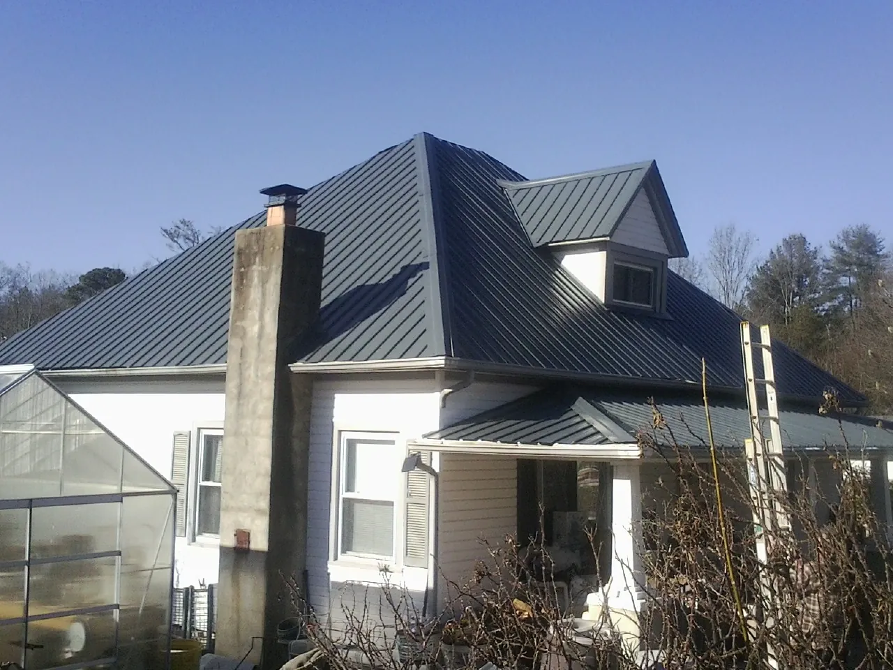 Dark blue standing seam metal roof on a white farmhouse with dormer — Slate & Tile Roof Repair by Roofing Brothers in New Liberty