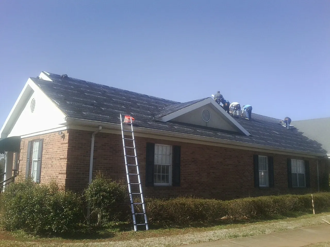 Crew tearing shingles off a brick ranch roof with a ladder set — Emergency Roof Repair work by our crew in New Liberty