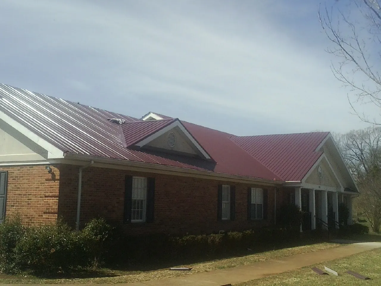 Red metal roof with gabled entries on a long brick building, from a Hail Damage Roof Repair job in New Liberty