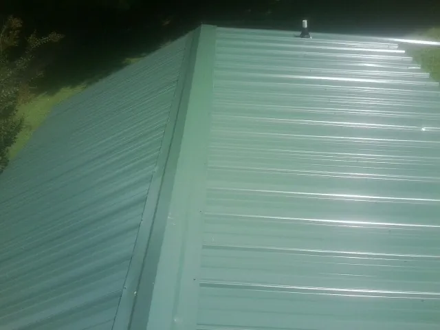 New green metal panels meeting at the ridge of a roof — Flat Roof Repair work by our crew in New Liberty