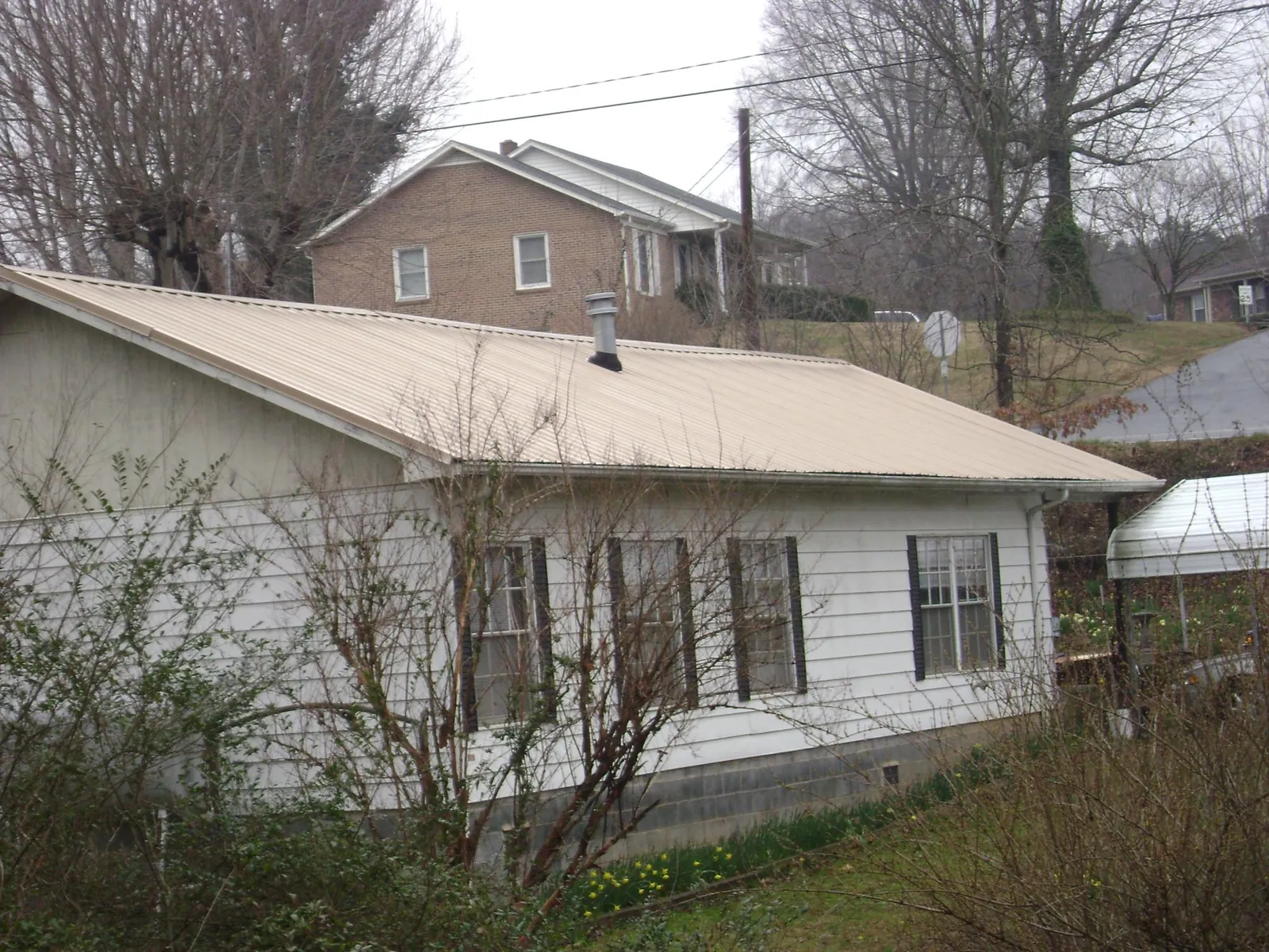 Tan metal roof on a white sided house set into a hillside — Commercial Roofing by Roofing Brothers in New Liberty